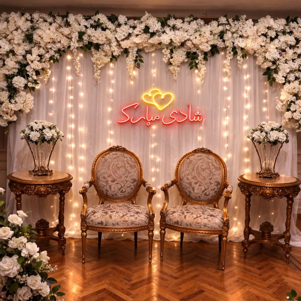 Decorative setup with floral arrangements, chairs, and a neon sign on a white curtain background.